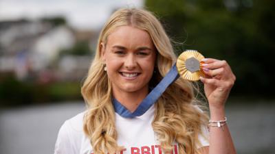 Hannah Scott holds her medal up to the camera. She wears her Team GB t shirt