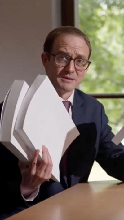 Chris Mason wears a suit holding a large pile of papers