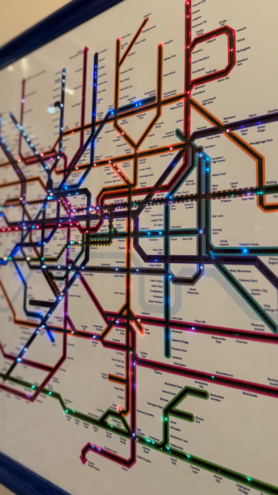 A framed map of the London transport network, with dozens of multicoloured LED lights tracking the live locations of individual services. 