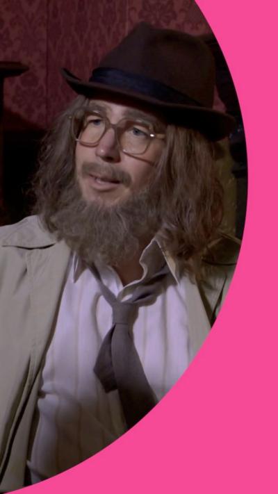 A man dressed in hat, fake beard and long hair, with a loose-fitting tie.