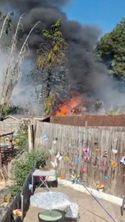 Flames and thick black smoke over a garden fence