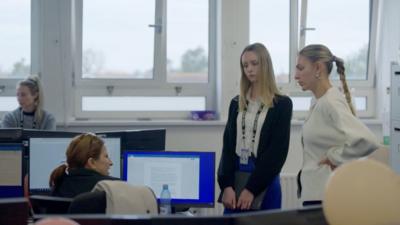 Two ladies speak to a third working at her computer