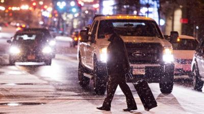 Man crosses the road in front of traffic with snow falling