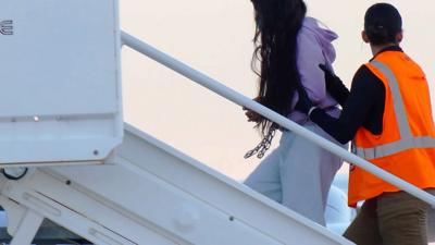 Woman in shackles being led onto a plane