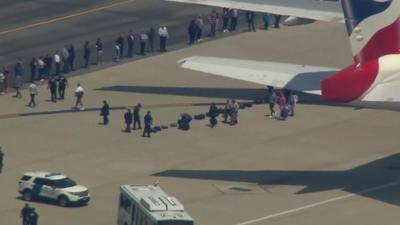 Shows passengers coming out of parked plane and putting their suitcases on the tarmac