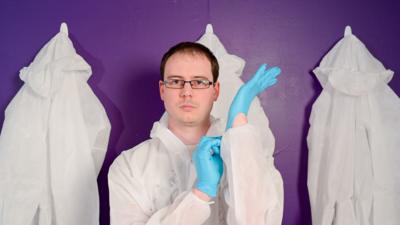 Man in white forensics suit pulls on a blue glove