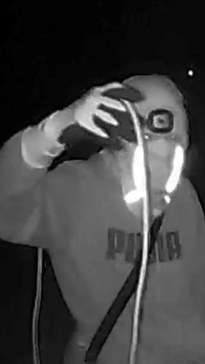 A black and white CCTV image of a man with a mask holding a coil of wire