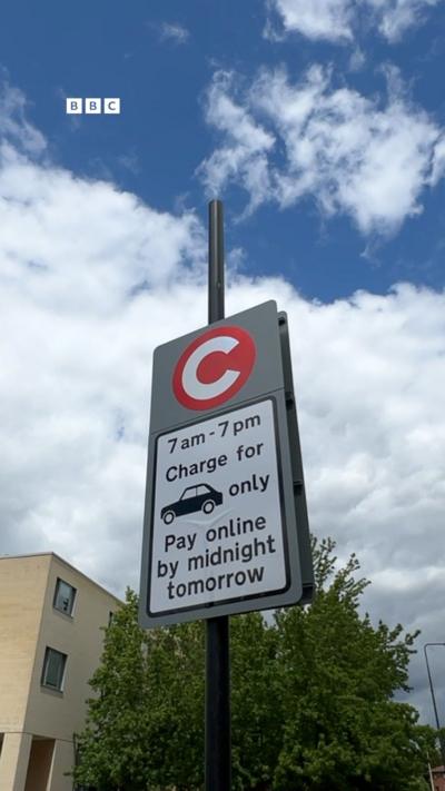 A congestion sign against a blue sky with clouds and a tree.