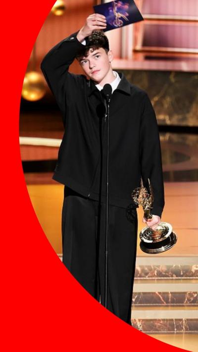 Cooper holds his award on stage and holds his hand to his head