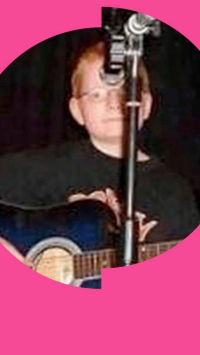 Ed Sheeran aged 11 stands in front of a mic holding a guitar, wearing glasses.