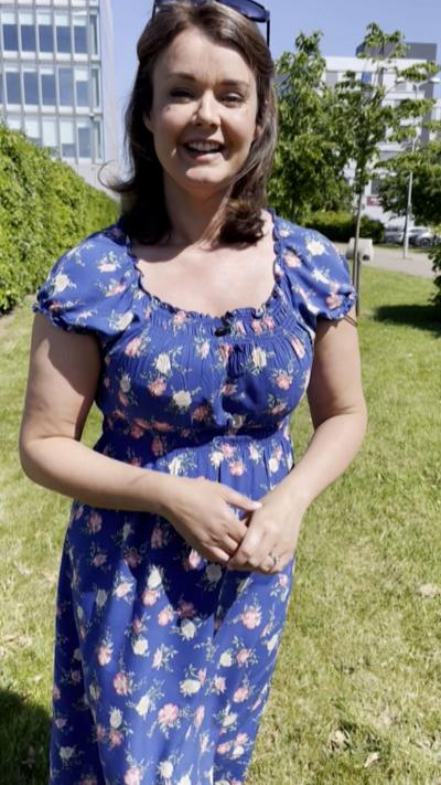 Woman in blue floral dress smiles as she stands outside on grass.