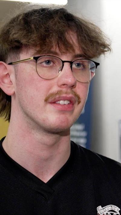 Young man with dark hair, black glasses and moustache, wearing a black tshirt