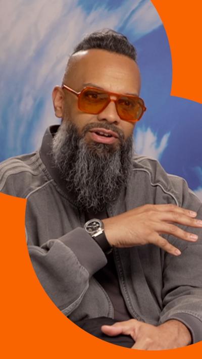 A man with orange shades and a long black beard raises his hand mid speech.