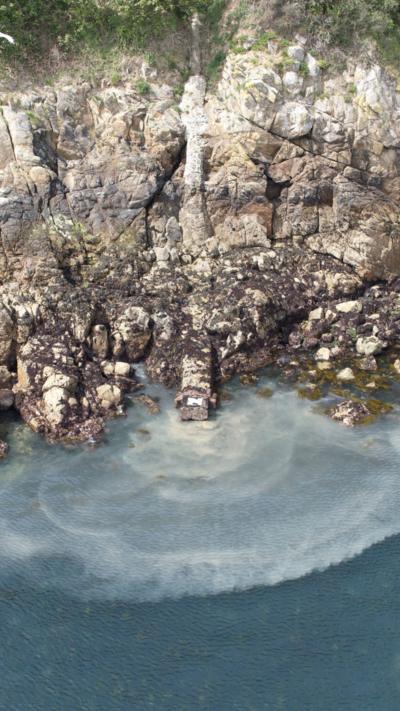 Raw sewage being discharged into the sea from a pipe down a cliff face