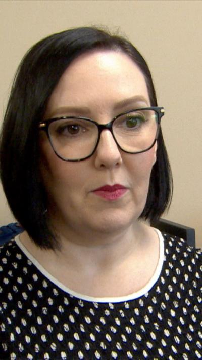 A woman with shoulder length black hair. She is wearing cateye black rimmed glasses and a black and white t-shirt. 