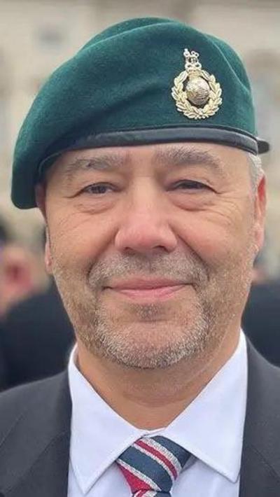 A Bearded man wearing a green beret, white shirt and royal marine tie beneath a dark jacket