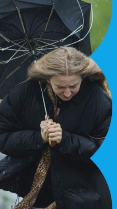 A woman struggling against wind and rain with an umbrella that has bent inside out