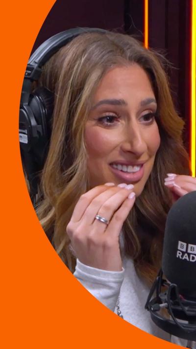 Woman with brown hair and headphones on her head holds her hands near her mouth.