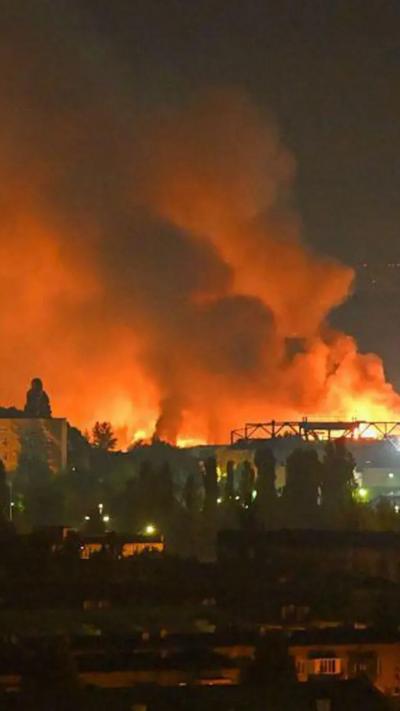 Large fire burning at night behind buildings and trees