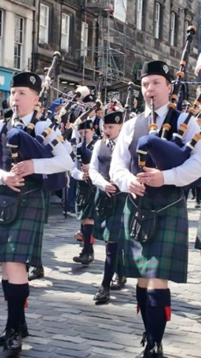 Members of a young pipe band wearing kilts playing as they walk down the Royal Mile, Edinburgh on a sunny day