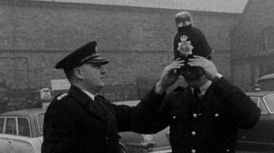 A police officer places a helmet with a flashing light on his head, with another police officer looking on.