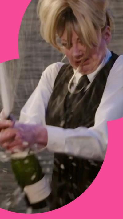 Mandy, in a waitress outfit, holding an exploding bottle of champagne 