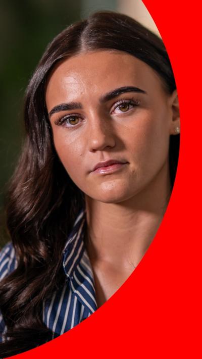 A woman with long brown hair has a sad expression. She is wearing a navy blue shirt with narrow white stripes.