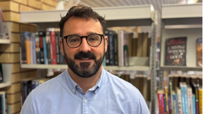 A man with black hair, beard and moustache and blue shirt 