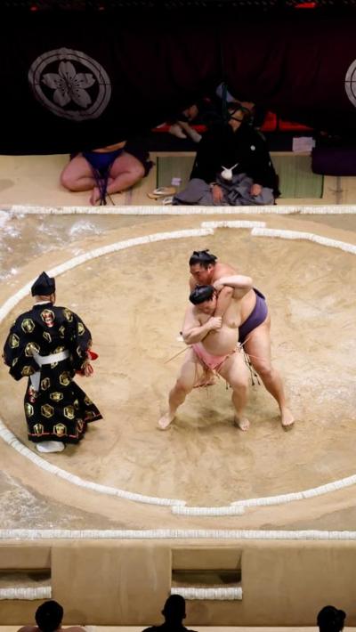 Referee watches two sumo wrestlers grappling