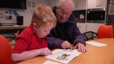 peter davies sat next to a student in a classroom reading a book together