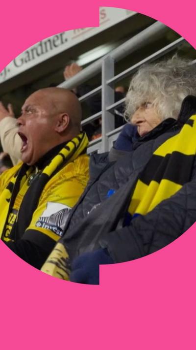 Miriam Margolyes watching the Hurricanes play in Wellington. She wears a black and yellow striped scarf