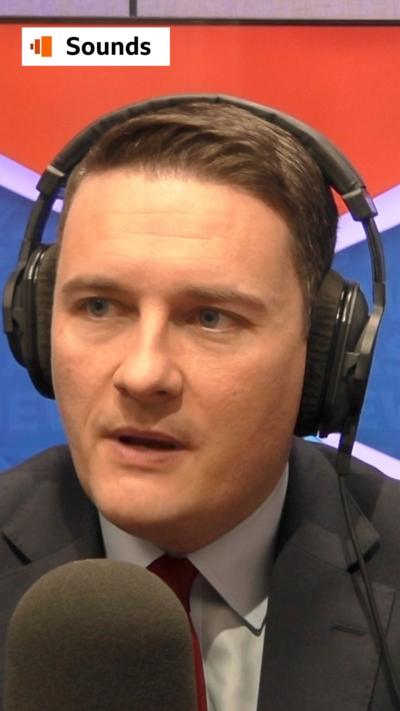 Wes Streeting speaking into a microphone wearing headphones