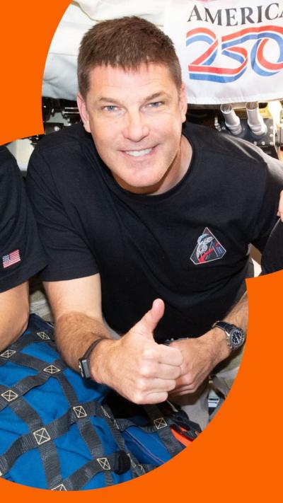 Astronaut Jeremy Hansen gives a thumbs up while onboard the Orion spacecraft. He is wearing a dark blue T-shirt.