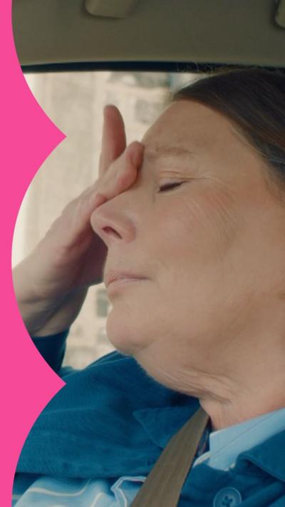 Character Beth sits in a car with her eyes closed and her hand on her forehead