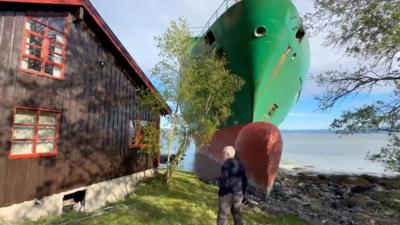 Man standing next to his house with large cargo ship washed up in his front garden