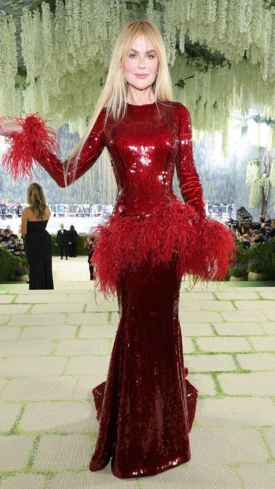 Nicole Kidman wears a long sequined red gown with feather details on the hips and wrists.