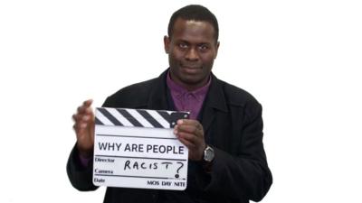 Man holds a clapper board saying "Why are people racist?"