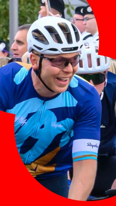 Chris Hoy smiles while wearing a cycle helmet, wraparound sunglasses and a blue cycling top