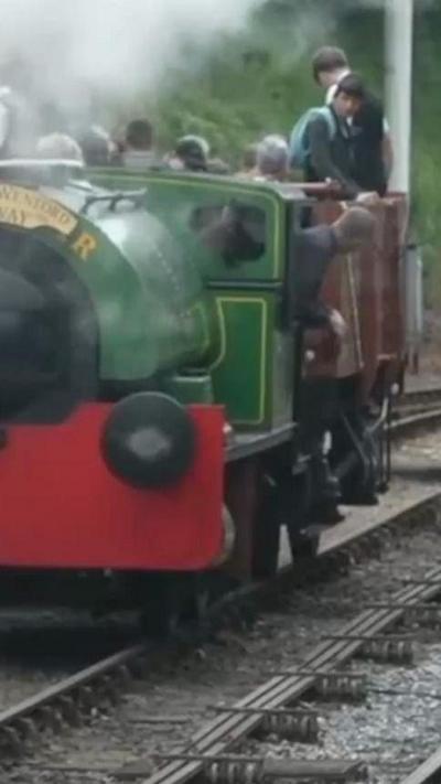 A green steam train on a track. There is steam coming out of the front of it. 