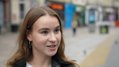 A young woman with brown hair in Cardiff city centre. She is looking to the right of the camera 