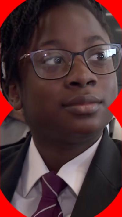 A young girl wearing school uniform, a white shirt and a black blazer. She has dark glasses.