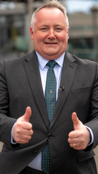 Darren Millar who has short grey hair in a suit with his thumbs up