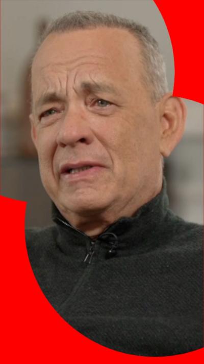 Tom Hanks, close up, wearing a black sweater. He's mid speech.