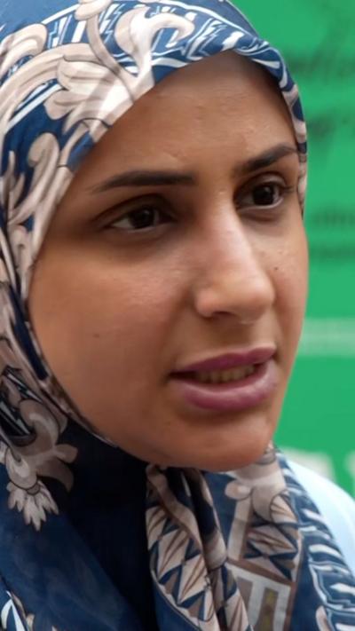 A woman wearingf a dark blue headscarf, with white patterns on it. 