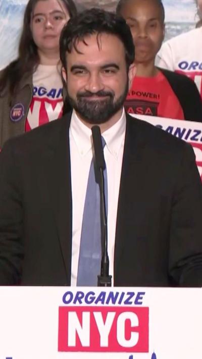 Zohran Mamdani standing at podium