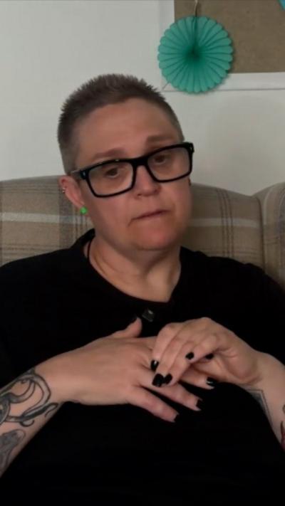 Woman with short dark hair and glasses sat on a sofa