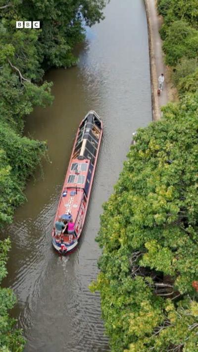 an aerial image of a red narrowboat on a canal
