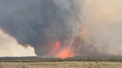 A dark cloud of smoke with a column of fire at its centre rises into the sky.
