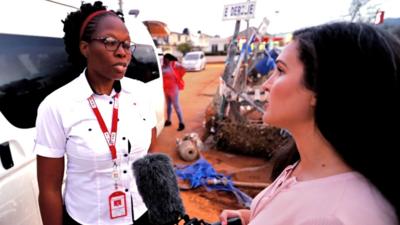 The BBC's Nada Tawfik, on the right, interviews a member of the Red Cross in front of a pile of hurricane debris.