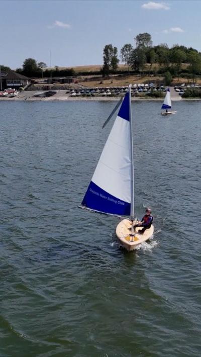 A sailing dinghy with a blue and white sail on a reservoir